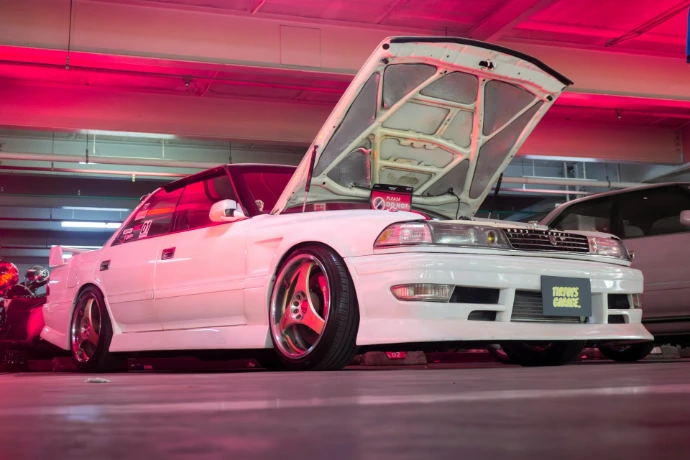 Modified white car with open hood in a red-lit garage.